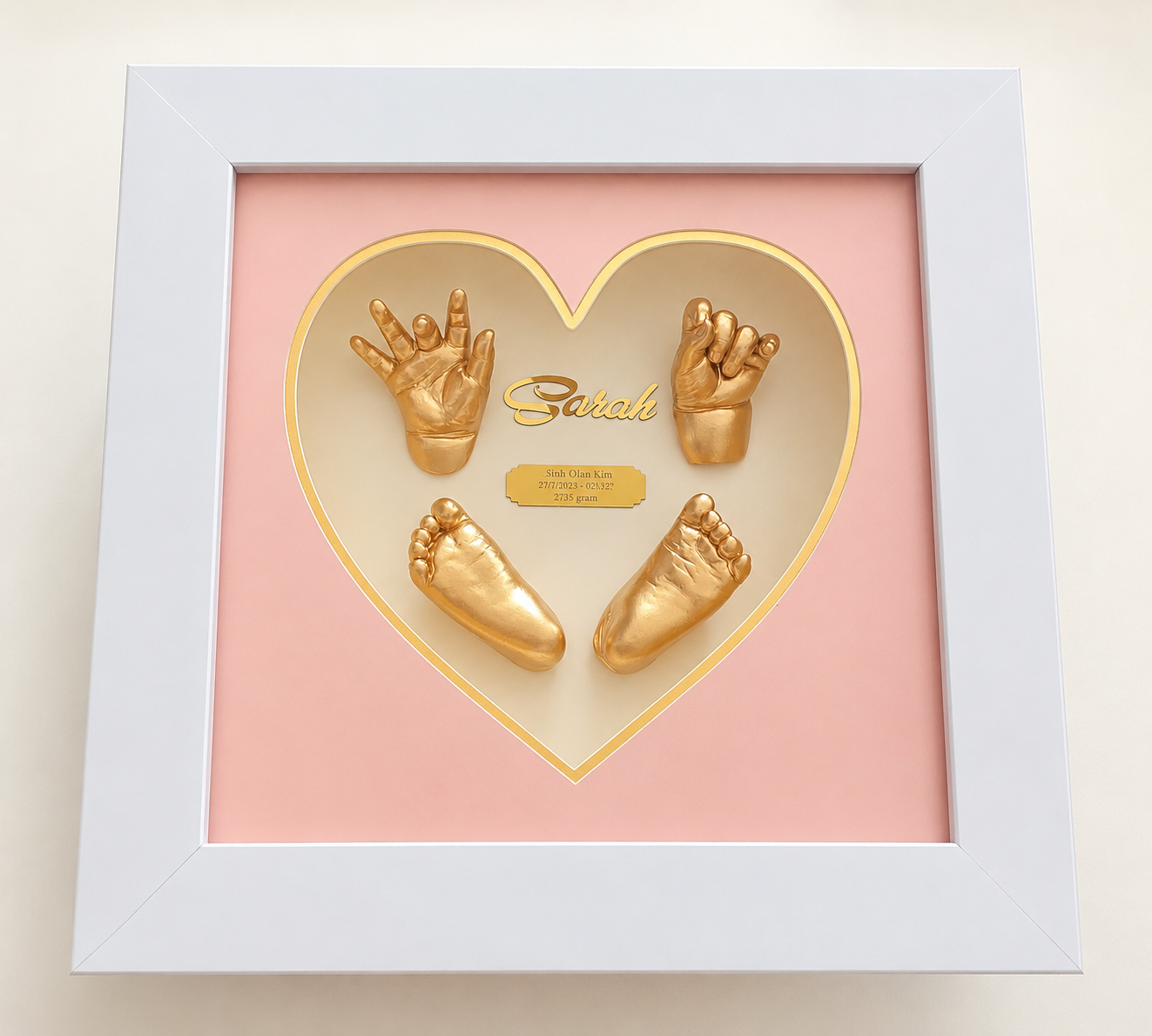 Mẫu tranh Baby Art được thiết kế với khung vuông trắng sang trọng, kích thước 30x30cm, nổi bật với mặt trái tim màu hồng nhẹ nhàng, tinh tế. Bên trong là dấu tay – dấu chân 3D của bé phủ vàng ánh kim, kết hợp cùng tên bé và thông tin ngày sinh, tạo nên tổng thể ấm áp, đáng yêu và đầy ý nghĩa. Sản phẩm phù hợp để lưu giữ kỷ niệm đầu đời của bé, trang trí không gian gia đình hoặc làm quà tặng đầy tháng, thôi nôi rất ý nghĩa